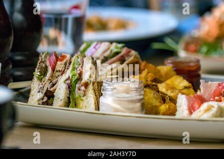 Ein Club Sandwich auf einem Teller mit Mayonnaise und Bratkartoffeln. Stockfoto