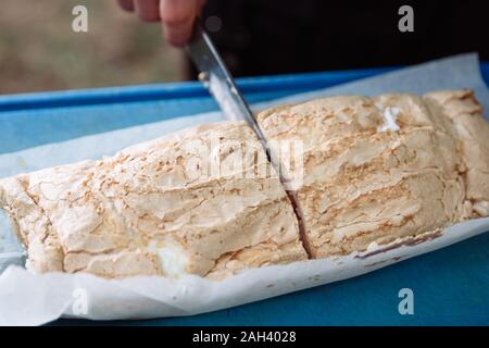 Koch schneidet in Portionen leckeren und frischen meringue Rolle mit Sahne. Stockfoto