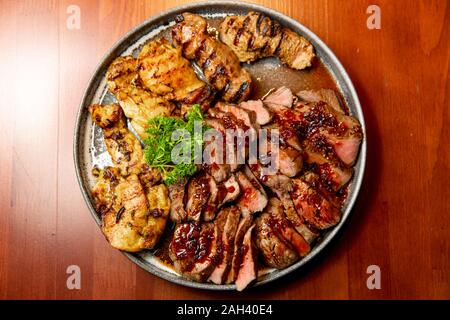 Frische, saftige Sortiment von geschnittenen Fleisch vom Grill, die auf eine große und runde Platte liegt, mit Petersilie auf der Oberseite dekoriert. Stockfoto