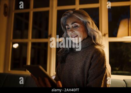 Reife Frau mit Tablet auf der Couch zu Hause in der Dunkelheit Stockfoto