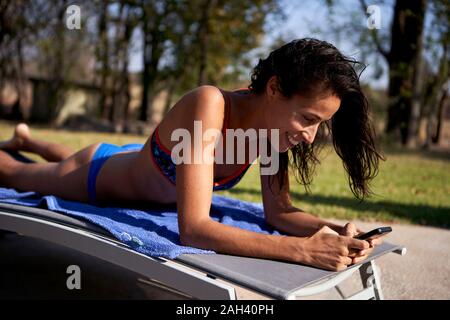 Glückliche Frau im Bikini liegen auf Sie ihr Smartphone Sonnenliege Stockfoto