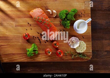 Set von gesunden Krebsnahrung auf Holztisch. Roter Lachsfisch, Brokkoli, Knoblauch, Milch, Pfeffer und Tomaten verstreut um den Tisch. Gesunde Mahlzeit Stockfoto