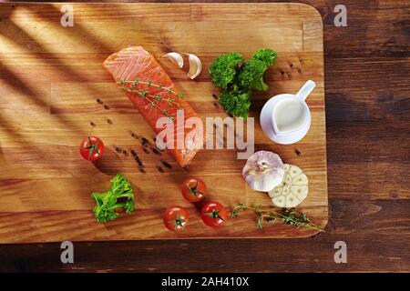 Set von gesunden Krebsnahrung auf Holztisch. Roter Lachsfisch, Brokkoli, Knoblauch, Milch, Pfeffer und Tomaten verstreut um den Tisch. Gesunde Mahlzeit Stockfoto