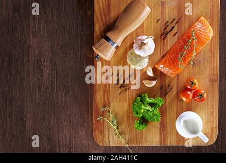 Set von gesunden Krebsnahrung auf Holztisch. Roter Lachsfisch, Brokkoli, Knoblauch, Milch, Pfeffer und Tomaten verstreut um den Tisch. Gesunde Mahlzeit Stockfoto