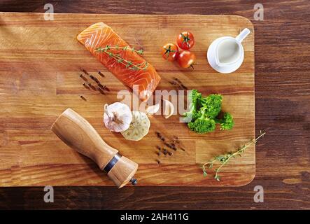 Set von gesunden Krebsnahrung auf Holztisch. Roter Lachsfisch, Brokkoli, Knoblauch, Milch, Pfeffer und Tomaten verstreut um den Tisch. Gesunde Mahlzeit Stockfoto