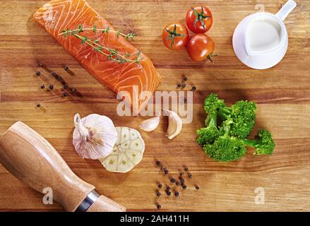 Set von gesunden Krebsnahrung auf Holztisch. Roter Lachsfisch, Brokkoli, Knoblauch, Milch, Pfeffer und Tomaten verstreut um den Tisch. Gesunde Mahlzeit Stockfoto