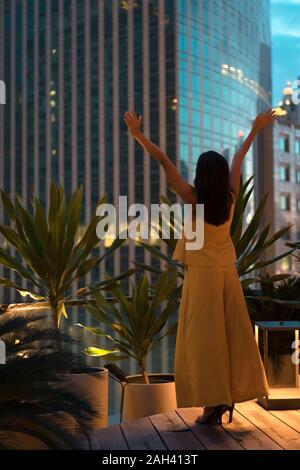 Rückansicht des glücklichen Frau, die auf der Dachterrasse heben die Hände, Bangkok, Thailand Stockfoto