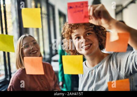 Gerne Kollegen mit Haftnotizen an der Glasscheibe im Büro Stockfoto