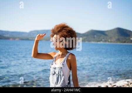 Junge Frau am Strand, Schirmung ihre Augen mit der Hand Stockfoto
