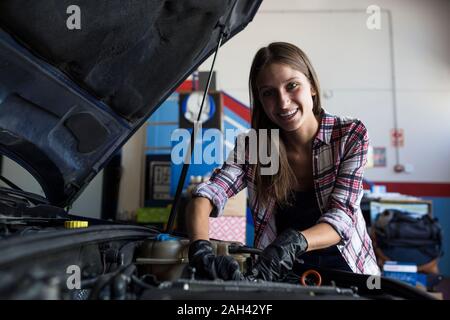 Junge casual lächelnde Frau an der Kamera, während die Festsetzung auto motor und Arbeiten in car service Stockfoto