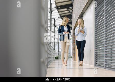Zwei junge Unternehmerinnen mit Tablet laufen und sprechen in der modernen Bürogebäude Stockfoto
