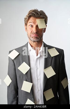 Portrait von hilflosen Geschäftsmann mit Hinweis Papiere stucking auf seiner Stirn und seinem Anzug Mantel Stockfoto