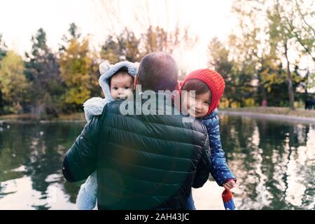 Porträt von zwei kleinen Mädchen auf's Vater Arme vor einem See bei Sonnenuntergang Stockfoto