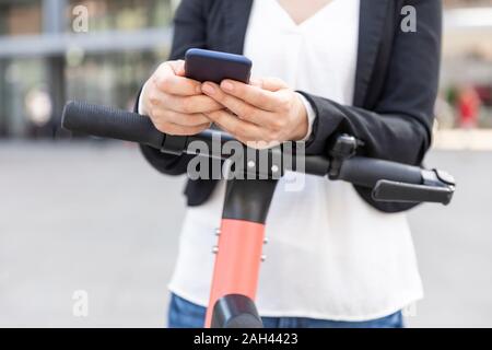 Frau, die mit dem Smartphone per E-Scooter in Berlin pendelt Stockfoto
