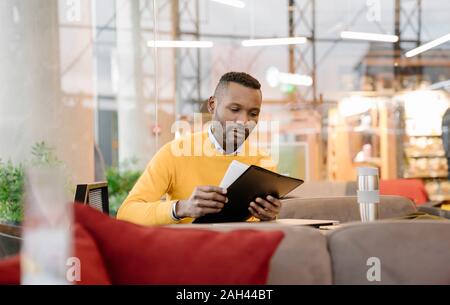 Mann mit wiederverwendbaren cup Lesen von Dokumenten in einem Cafe Stockfoto