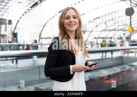 Porträt der lächelnde Frau mit Smartphone am Bahnhof, Berlin, Deutschland Stockfoto