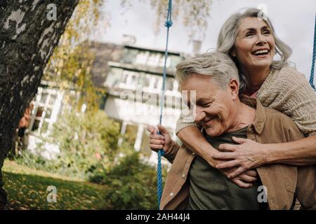 Glückliche Frau umarmt älterer Mann auf einer Schaukel im Garten Stockfoto