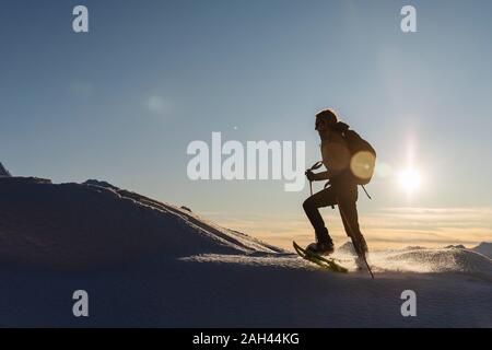 Frau wandern mit Schneeschuhen in den frischen Schnee in die Berge bei Sonnenuntergang, Valmalenco, Italien Stockfoto