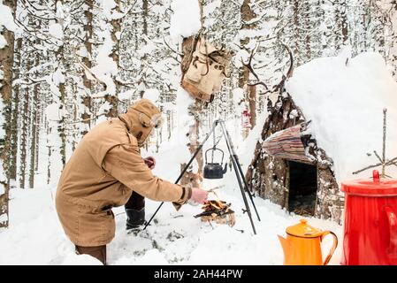 Mann die Zubereitung von Tee im Winter Wald neben einem hölzernen Unterstand, Salzburg Land, Österreich Stockfoto