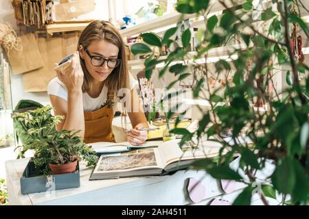 Junge Frau mit Smartphone Notizen in einem kleinen Garten shop Stockfoto