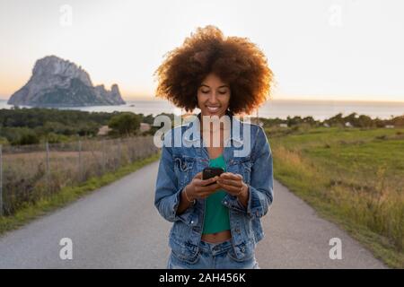 Junge Frau auf einer Straße mit Smartphone, Ibiza Stockfoto