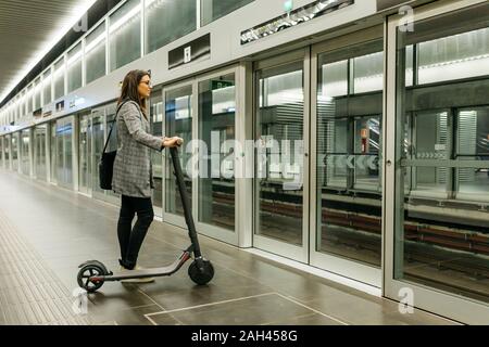 Junge Geschäftsfrau mit e-Scooter warten auf die U-Bahn an einer Station Stockfoto