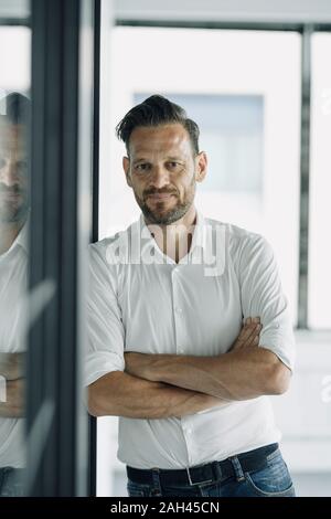 Portrait von zuversichtlich reife Geschäftsmann lehnte sich gegen Glaswand im Büro Stockfoto