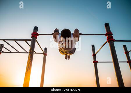 Junger Mann üben calisthenics an ein Fitnessbereich im Freien bei Sonnenaufgang Stockfoto