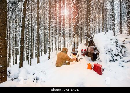 Mann die Zubereitung von Tee im Winter Wald neben einem hölzernen Unterstand, Salzburg Land, Österreich Stockfoto