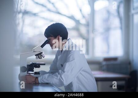 Weibliche Chemiker, der durch ein Mikroskop Stockfoto