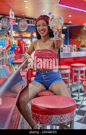 Junge Frau mit geflochtenem Frisur sitzen auf eine Bar, einen Toast mit Ihren Cocktail Stockfoto