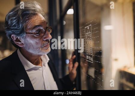 Senior Geschäftsmann an der Zeichnung auf der Glasscheibe im Büro suchen Stockfoto