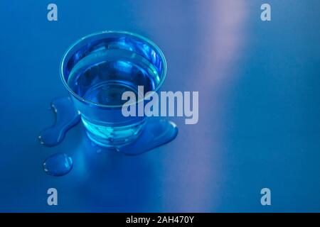 Gefüllte blaue Glas Wasser auf Blau neon Hintergrund mit Wasser darauf verschüttet. Kopieren Sie Platz. Stockfoto