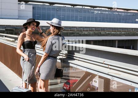 Zwei modischen jungen Frauen mit Gepäck am Flughafen sprechen Stockfoto