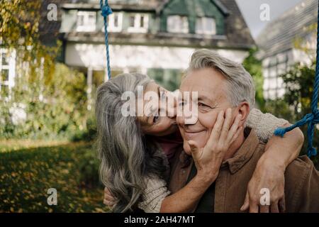 Glückliche Frau umarmen, küssen ein älterer Mann auf einer Schaukel im Garten Stockfoto