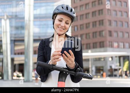 Frau mit e-Scooter mit in der Stadt smartphone, Berlin, Deutschland Stockfoto