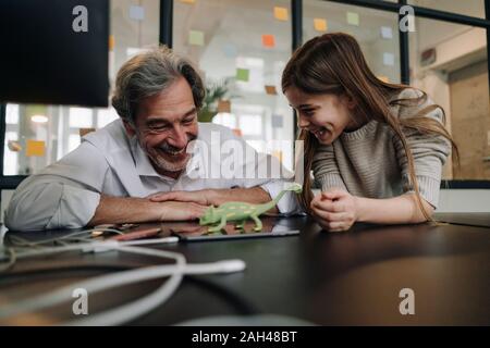 Happy senior buisinessman und Mädchen spielen mit Chameleon Figur im Büro Stockfoto