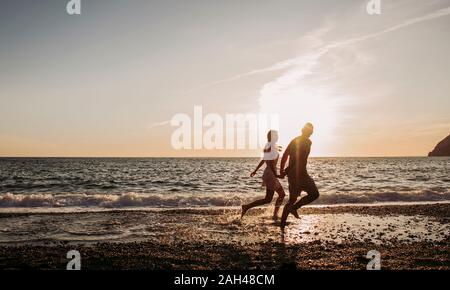 Junges Paar laufen am Strand bei Sonnenuntergang Stockfoto