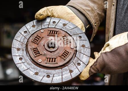 Automechaniker in Arbeitsschutzhandschuhen, hält verwendet Kupplungsscheibe. Kupplungsscheibe Reibbeläge. Close-up. Augenhöhe schießen. Stockfoto