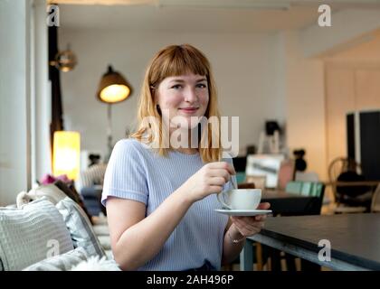 Portrait von Strawberry blonde junge Frau mit Nasenpiercing mit Tasse Kaffee in einem Cafe Stockfoto