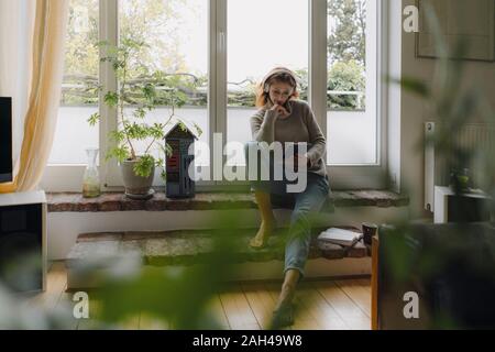 Reife Frau sitzt auf der Fensterbank wondow, mit digitalen Tablet Stockfoto