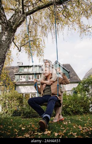 Glückliche Frau umarmt älterer Mann auf einer Schaukel im Garten Stockfoto