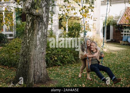 Glückliche Frau umarmt älterer Mann auf einer Schaukel im Garten Stockfoto