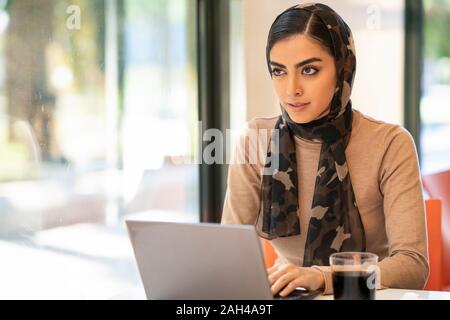 Junge Frau mit Kopftuch mit Laptop in einem Cafe Stockfoto
