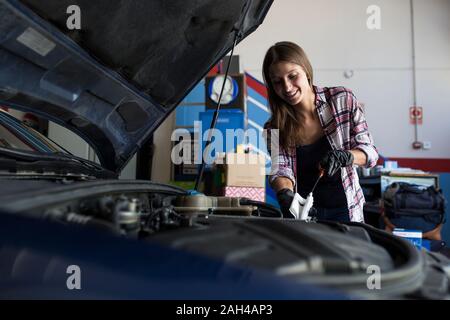 Junge casual Frau in T-Shirt und Handschuhe arbeiten mit Auto in Reparatur Service Prüfung des Motorölstands Stockfoto