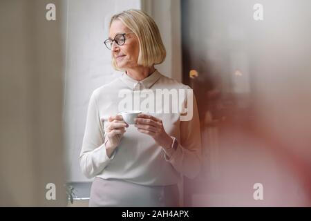 Reife Geschäftsfrau mit einer Kaffeepause am Fenster im Büro Stockfoto