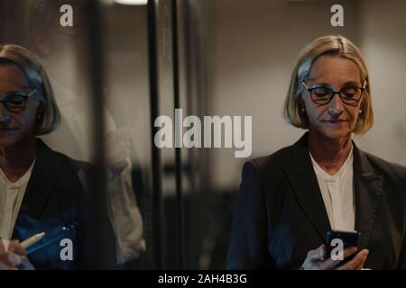 Reife Geschäftsfrau mit Smartphone in der Glasscheibe officereflected Stockfoto