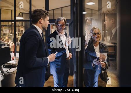 Lächelnd Geschäftsfrau und zwei Geschäftsleute, die auf der Zeichnung auf der Glasscheibe im Büro Stockfoto