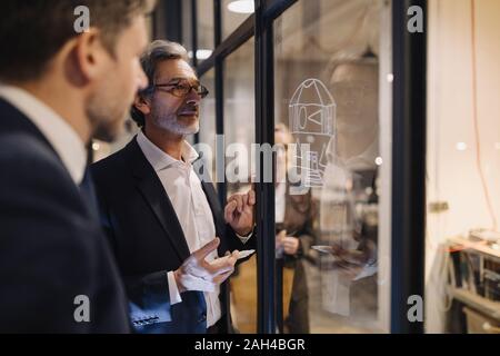 Zwei Geschäftsleute arbeiten auf der Zeichnung auf der Glasscheibe im Büro Stockfoto