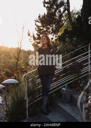 Glückliche Frau, die auf der Treppe in Ihrem Garten, lächelnd Stockfoto